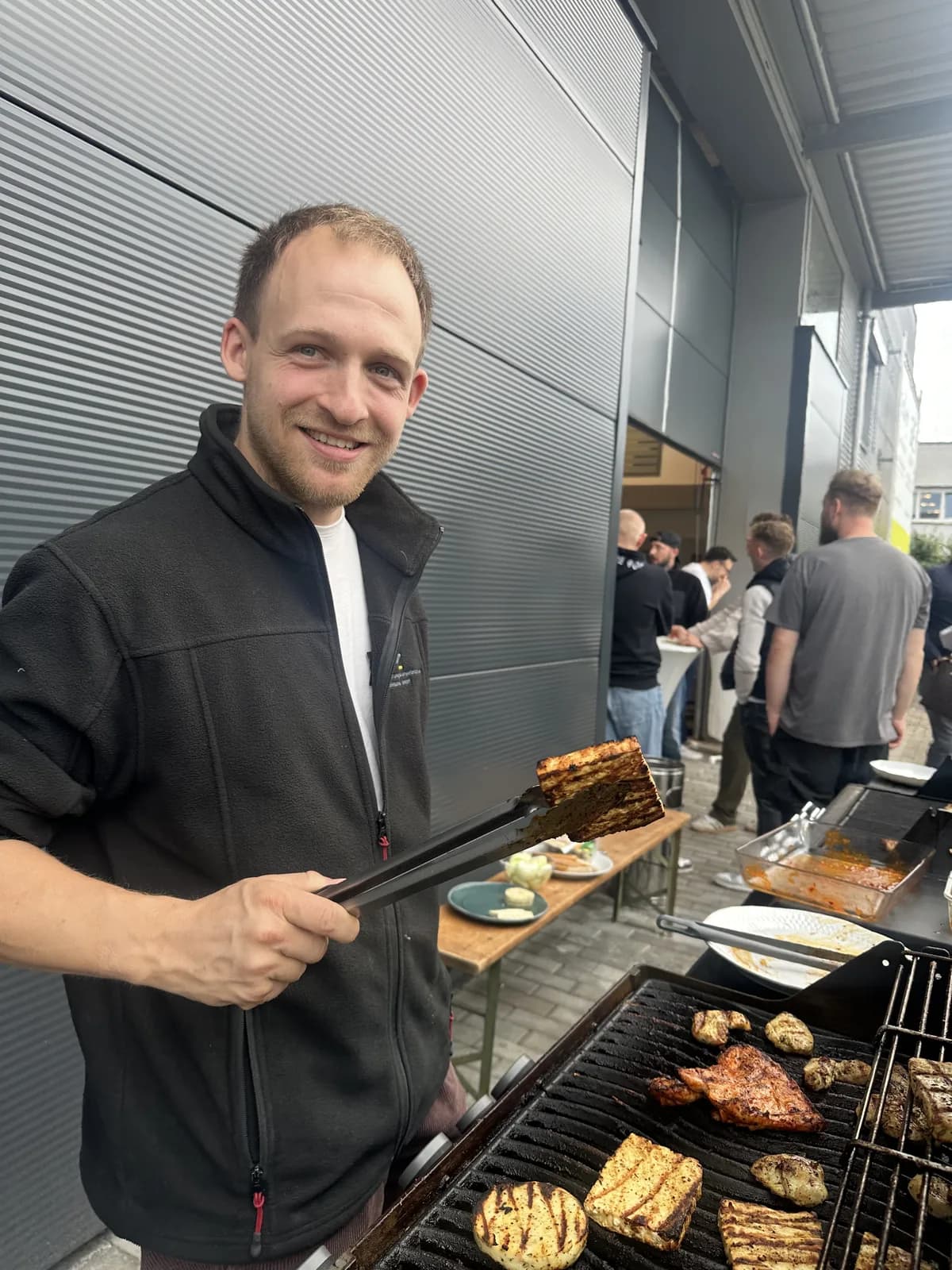 Kollege von SKZ Rheinland mit Grillzange am Grill vor der Halle beim Sommerfest 2026