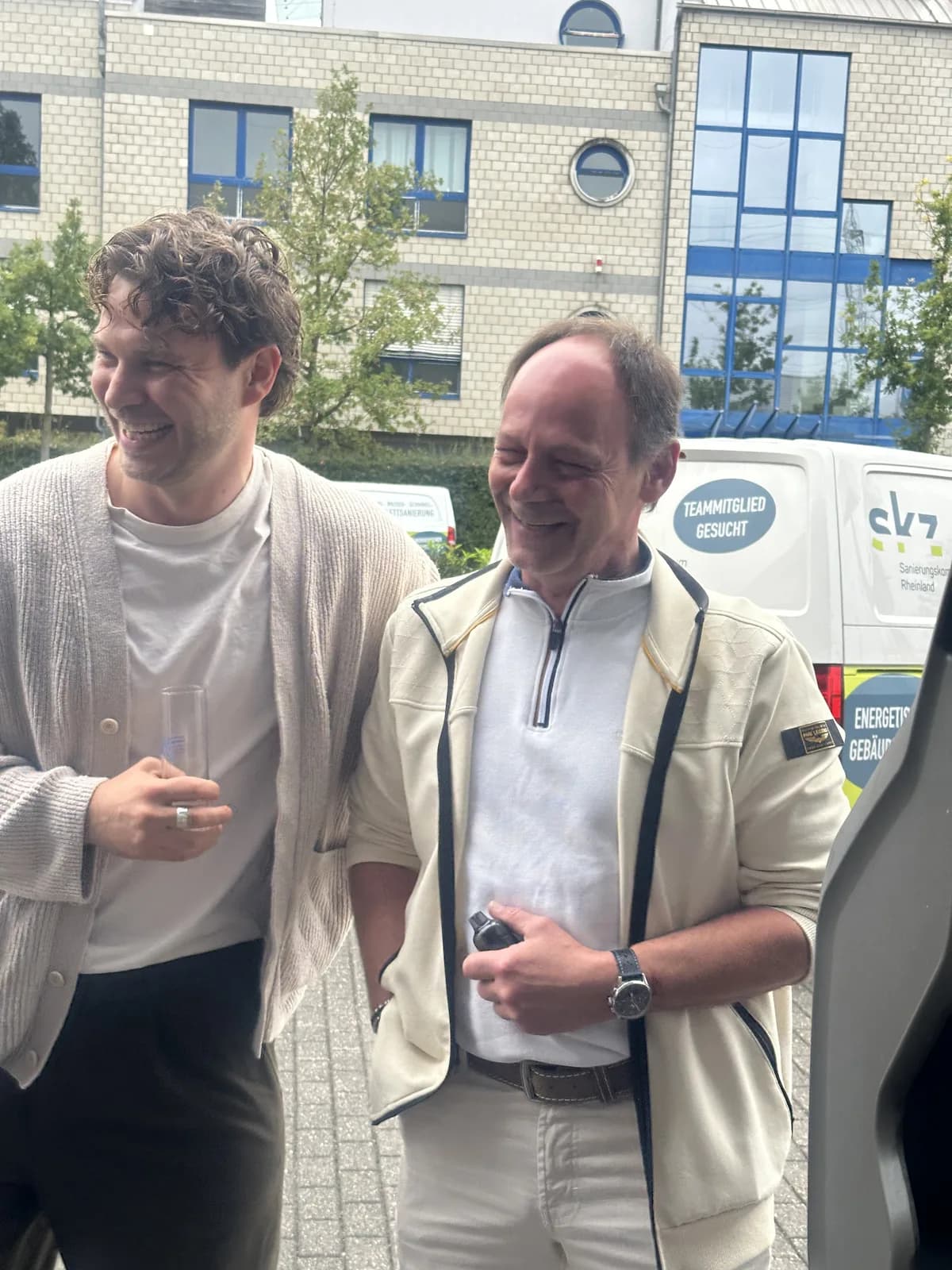 Zwei lachende Kollegen vor einem SKZ-Transporter mit der Aufschrift „Teammitglied gesucht“